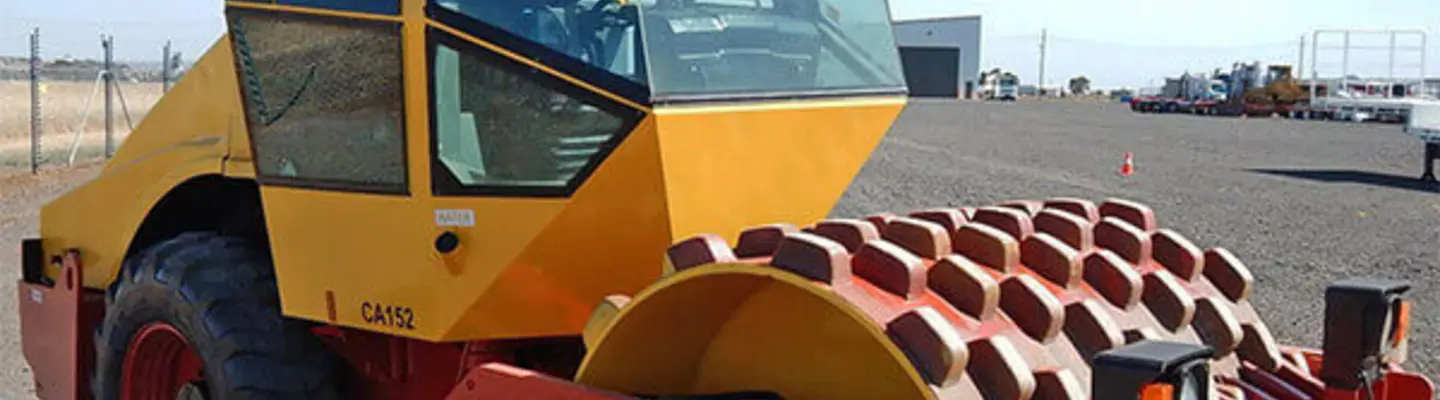 Picture of a roller machine on a construction site, surrounded by safety barriers and signage for hazard prevention.
