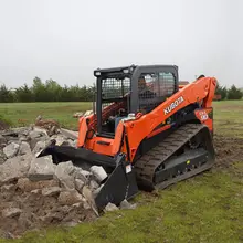 A truck loader actively digging and moving rocks at a construction site, with safety barriers visible in the background.