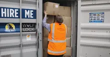 Worker in a high-visibility vest loading cardboard boxes into a storage container.