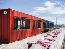 Kiosk made from a shipping container with tables and chairs set up outside, creating a casual outdoor seating area.